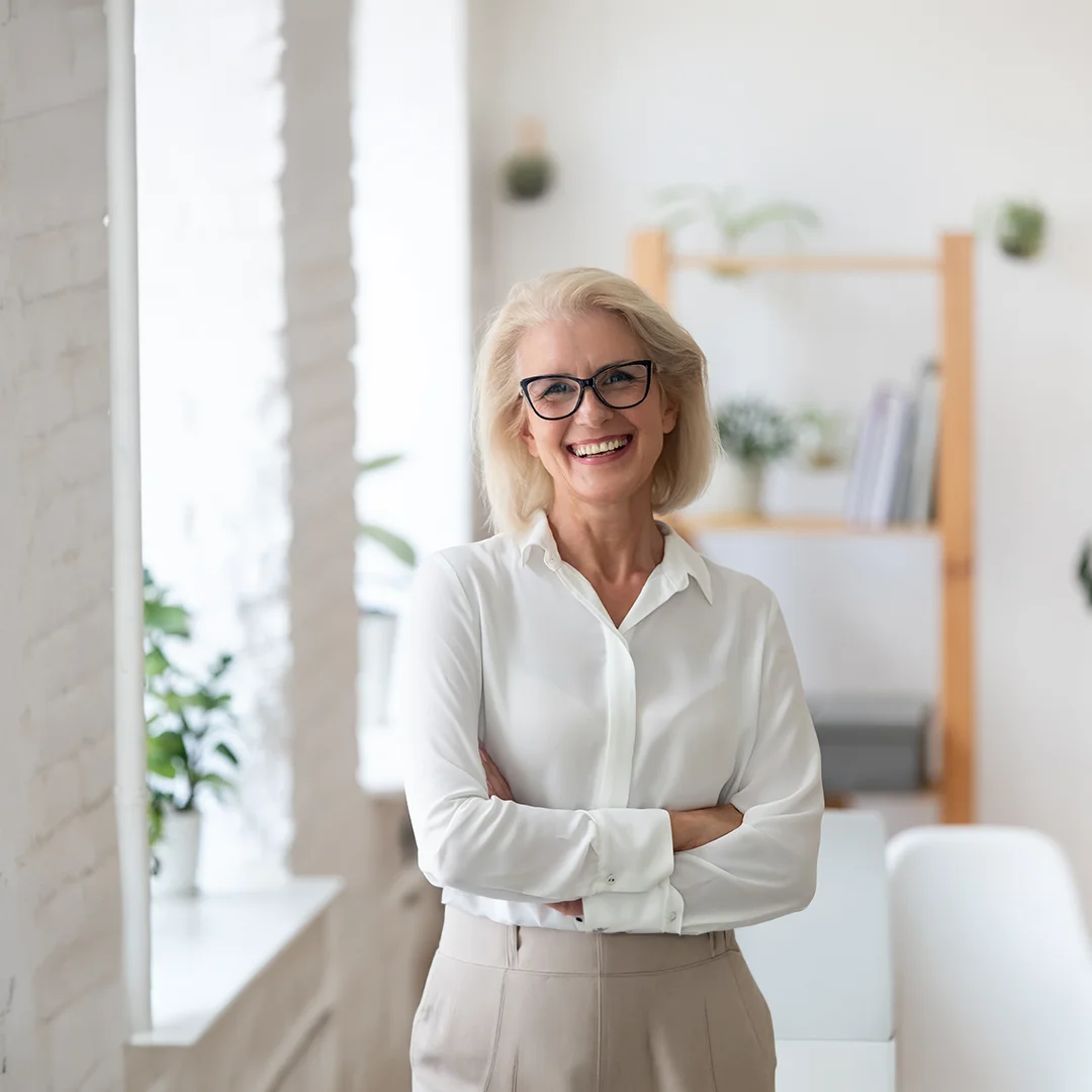 Confident executive coach smiling with arms crossed in a bright office, representing leadership coaching and professional development