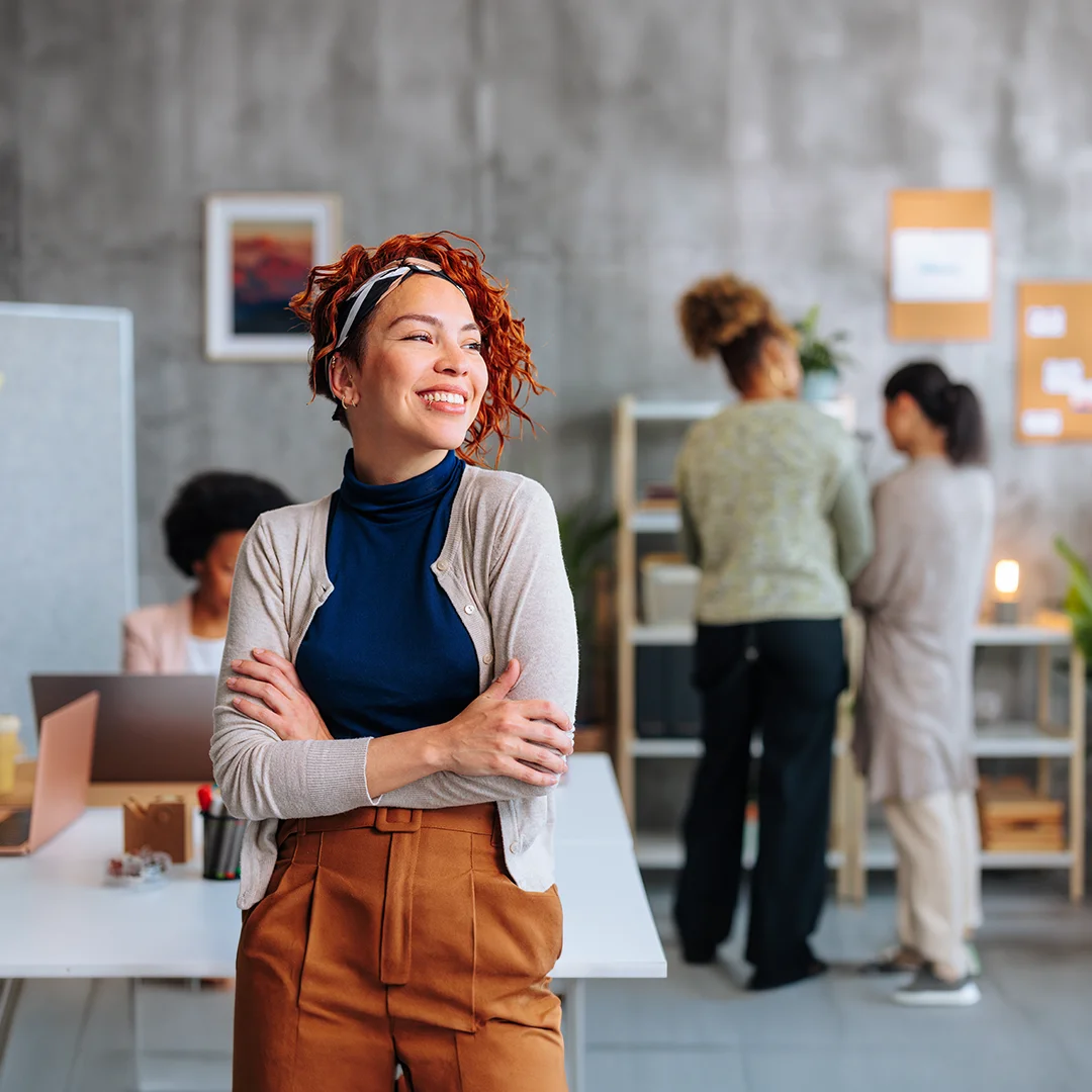 Confident professional woman smiling in a collaborative workspace, representing leadership coaching, workplace culture, and team development